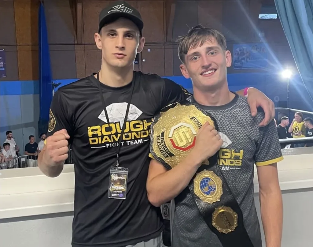 My son holding two championship belts beside a teammate after winning the title