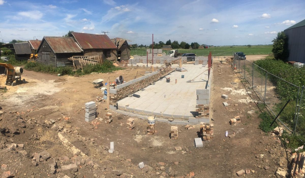 Early construction of our rural self-build, with a concrete floor, partially built block walls, scattered bricks and farm buildings around the site