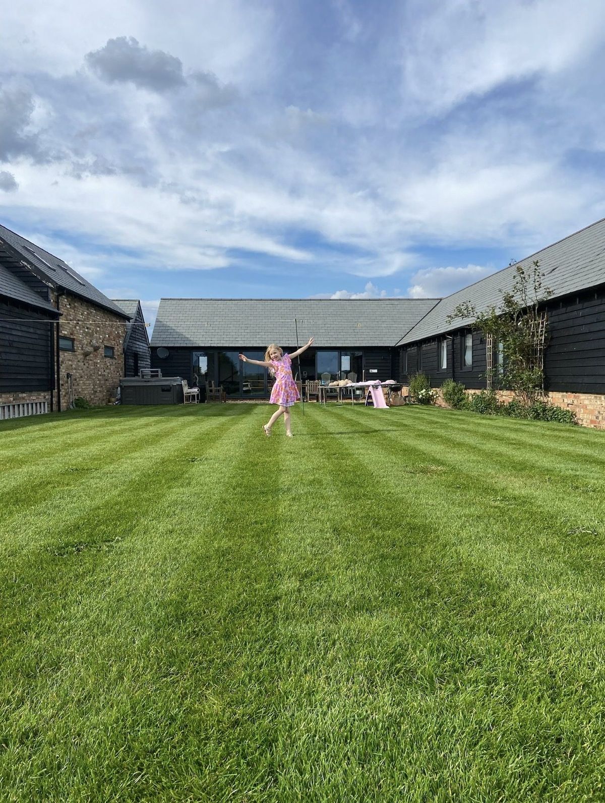 Our completed black timber home surrounding a broad green lawn, with a child playing beneath a wide summer sky
