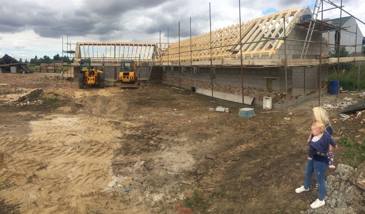 Our self-build taking shape with timber roof trusses, scaffolding and machinery, while family life continues at the edge of the muddy site